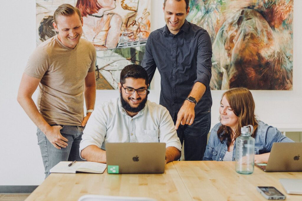 Cuatro compañeros sonriendo alrededor de una laptop